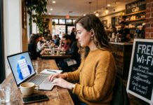Hackers Love Public Wi-Fi: 7 Mistakes That Put Your Data at Risk A woman wearing earbuds works on a laptop at a wooden table in a busy cafe
